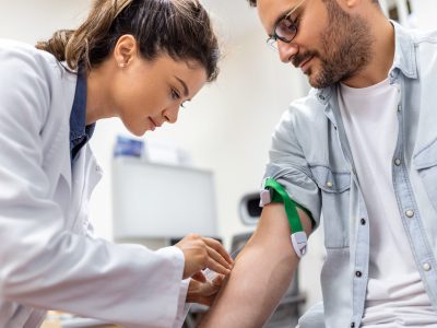 Friendly hospital phlebotomist collecting blood sample from patient in lab. Preparation for blood test by female doctor medical uniform on the table in white bright room Friendly hospital phlebotomist collecting blood sample from patient in lab. Preparation for blood test by female doctor medical uniform on the table in white bright room
