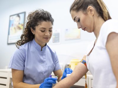 Medical technologist doing a blood draw services for patient. lab assistant with sterile rubber gloves taking blood sample from patient.